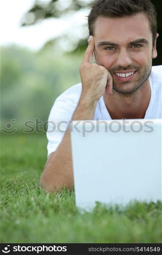 Man laying in the park surfgin the internet