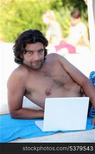 Man laying on beach towel with laptop