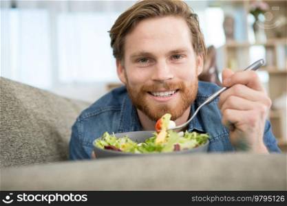 man laying on the sofa eating a salad