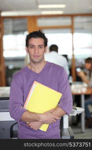 Man leaning against a photocopier with a armful of files