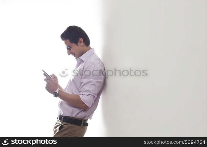 Man leaning against a wall reading an sms