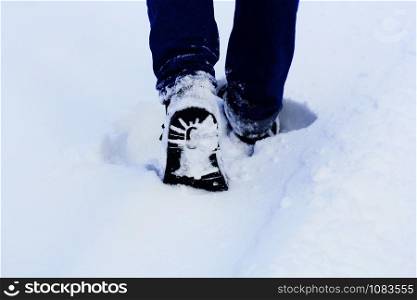 Man legs in winter shoes walking on snow covered path . Close -up .
