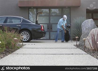 Man lifting golf bag into boot of luxury vehicle