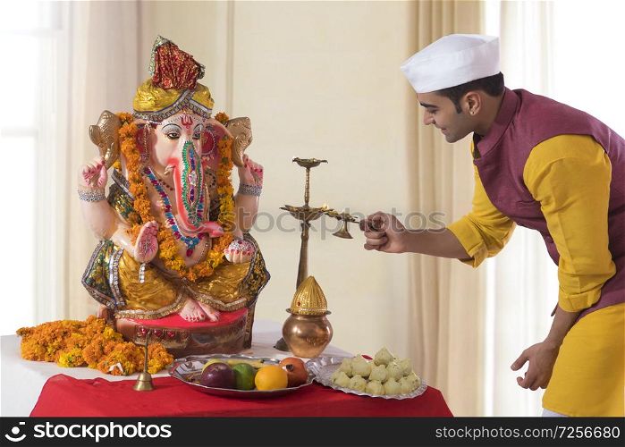 Man lighting the diya in front of Ganesh Idol for Ganesh Chaturthi Pooja