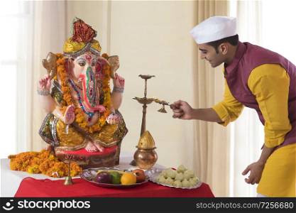 Man lighting the diya in front of Ganesh Idol for Ganesh Chaturthi Pooja