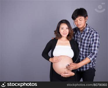 man listening the belly of his pregnant wife with stethoscope on gray wall background&#xA;&#xA;stethoscope