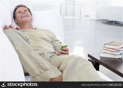 Man listening to MP3 player on sofa in living room