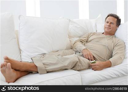 Man listening to MP3 player on sofa in living room portrait