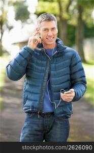 Man Listening To MP3 Whilst Walking In Autumn Park
