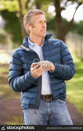 Man Listening To MP3 Whilst Walking In Autumn Park