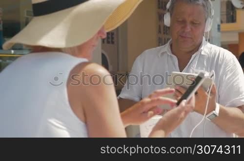 Man listening to music on his tablet and showing something to his wife who using smartphone. Summertime.