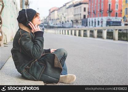 Man listening to music through headphones on kerb, Milan, Italy