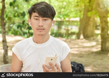 Man listening to music with a smartphone standing in the park.