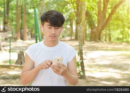 Man listening to music with a smartphone standing in the park.