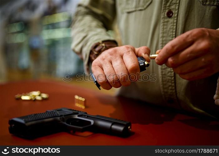 Man loads the magazine with bullets in gun store. Weapon shop interior, ammo and ammunition assortment, firearms choice, shooting hobby and lifestyle, self protection. Man loads the magazine with bullets in gun store