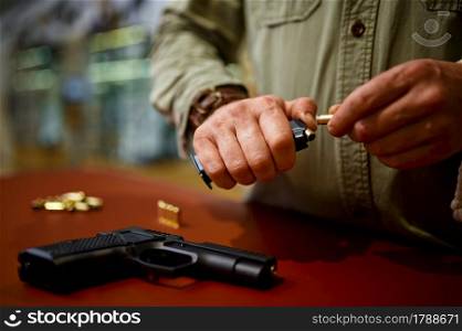 Man loads the magazine with bullets in gun store. Weapon shop interior, ammo and ammunition assortment, firearms choice, shooting hobby and lifestyle, self protection. Man loads the magazine with bullets in gun store