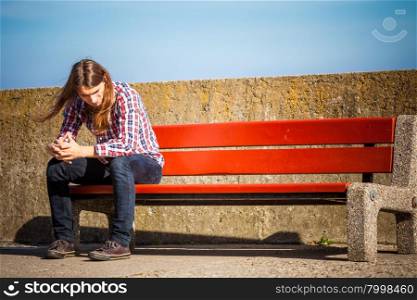 Man long hair alone on bench, lost in thought, is concerned and stressed about events in his life. Unemployment depression concept