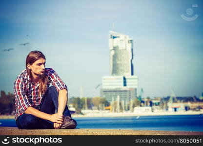 Man long hair relaxing by seaside . Man bearded long hair wearing plaid shirt casual style relaxing by seaside at summer sunny windy day