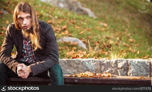 Man long hair sad thoughtful sitting on bench outdoor in autumnal park. Man long hair sitting on bench in autumn park