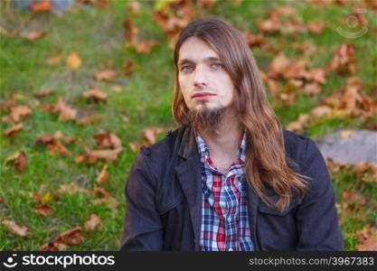 Man long hair sitting on bench in autumn park. Man long hair sad thoughtful sitting on bench outdoor in autumnal park