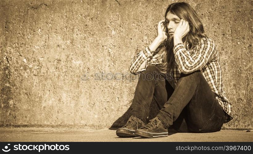 Man long haired sitting alone sad on grunge wall. Man bearded long hair sitting sad alone by grunge wall outdoor. Unemployment depression or sadness concept.
