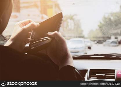 Man look at his empty wallet while driving car, dangerous behavior