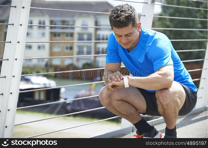 Man Looking At Activity Tracker Whilst Exercising In City