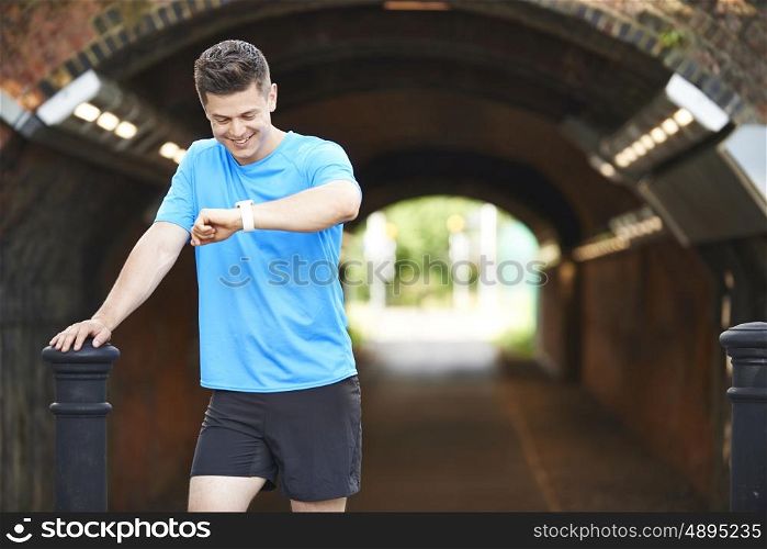 Man Looking At Activity Tracker Whilst Exercising In Urban Setting
