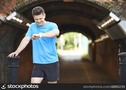 Man Looking At Activity Tracker Whilst Exercising In Urban Setting