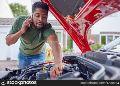 Man Looking At Engine After Car Breakdown Calling Auto Recovery On Mobile Phone