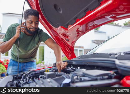 Man Looking At Engine After Car Breakdown Calling Auto Recovery On Mobile Phone