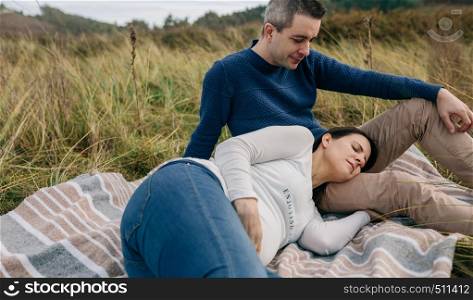 Man looking at his pregnant woman resting on a blanket on the grass. Man looking his pregnant woman resting on the grass