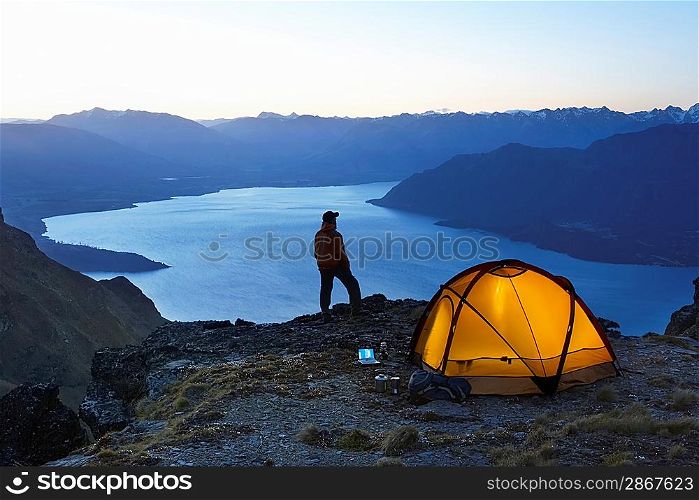 Man looking at lake next to tent at dusk