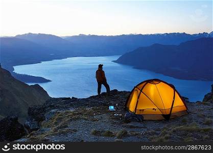Man looking at lake next to tent at dusk