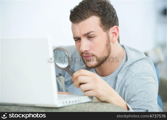man looking at laptop through magnifying glass