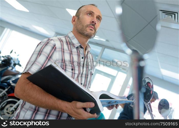 man looking at notes while examining motorbikes in a salon