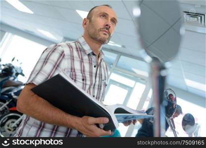 man looking at notes while examining motorbikes in a salon