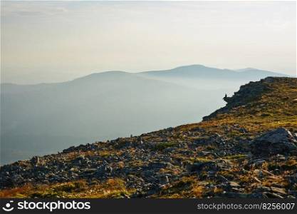 Man looking at sunrise. Mountains at sunrise. Man standing on peak. Natural mountain landscape with illuminated misty peaks, foggy slopes and valleys, blue sky with orange yellow sunlight. Amazing scene from Beskid Zywiecki in Poland