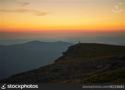 Man looking at sunrise. Mountains at sunrise. Man standing on peak. Natural mountain landscape with illuminated misty peaks, foggy slopes and valleys, blue sky with orange yellow sunlight. Amazing scene from Beskid Zywiecki in Poland