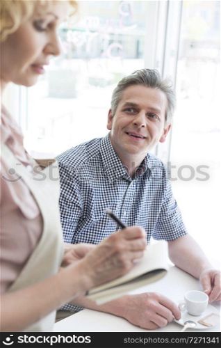 Man looking at waitress writing order on notepad at restaurant