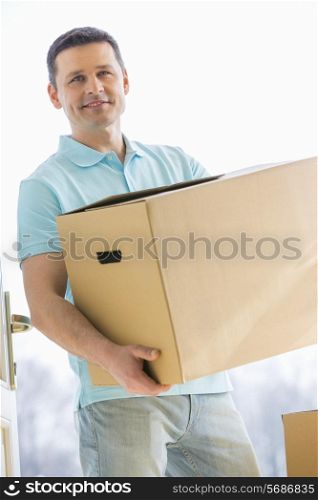 Man looking away while carrying cardboard box while entering new house