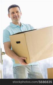 Man looking away while carrying cardboard box while entering new house