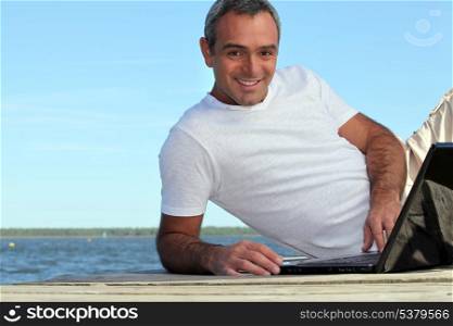 Man looking his laptop by the lake