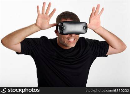 Man looking in VR glasses and gesturing with his hands. Beautiful surprised guy wearing virtual reality goggles watching movies or playing video games, isolated on white background.