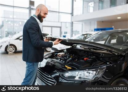 Man looking on transport engine in car dealership. Customer in new vehicle showroom, male person buying automobile, auto dealer business. Man looking on transport engine in car dealership