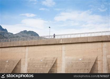 Man looking the views from the top of a lake dam