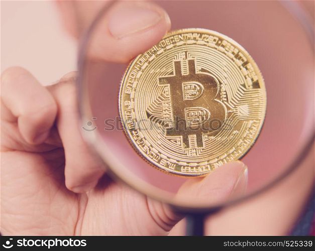 Man looking through magnifying glass at bitcoin crypto internet currency. Trying to figure out net banking. Man looking at bitcoin through magnifying glass