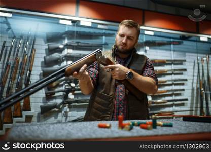 Man looks on rifle barrel at counter in gun shop. Euqipment for hunters on stand in weapon store, hunting and sport shooting hobby. Man looks on rifle barrel at counter in gun shop