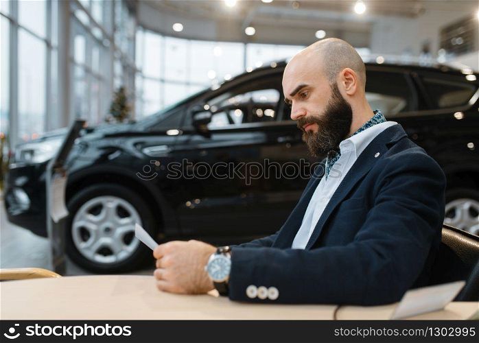Man looks price on new automobile in car dealership. Customer in vehicle showroom, male person buying transport, auto dealer business. Man looks price on new automobile, car dealership