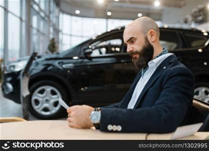Man looks price on new automobile in car dealership. Customer in vehicle showroom, male person buying transport, auto dealer business. Man looks price on new automobile, car dealership